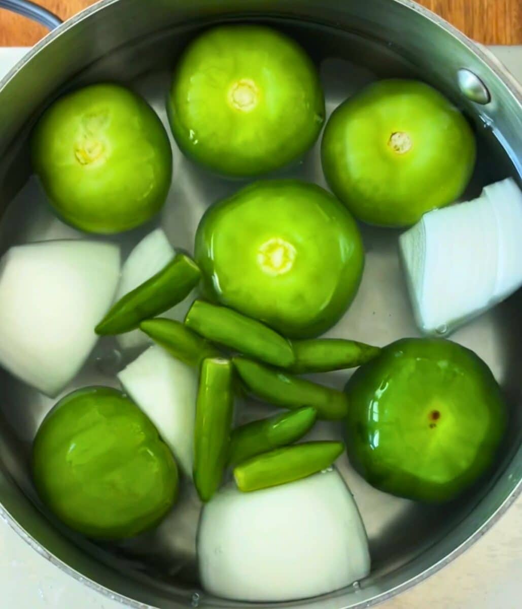 Tomatillo, onion, garlic, and serrano peppers in a pot with water.