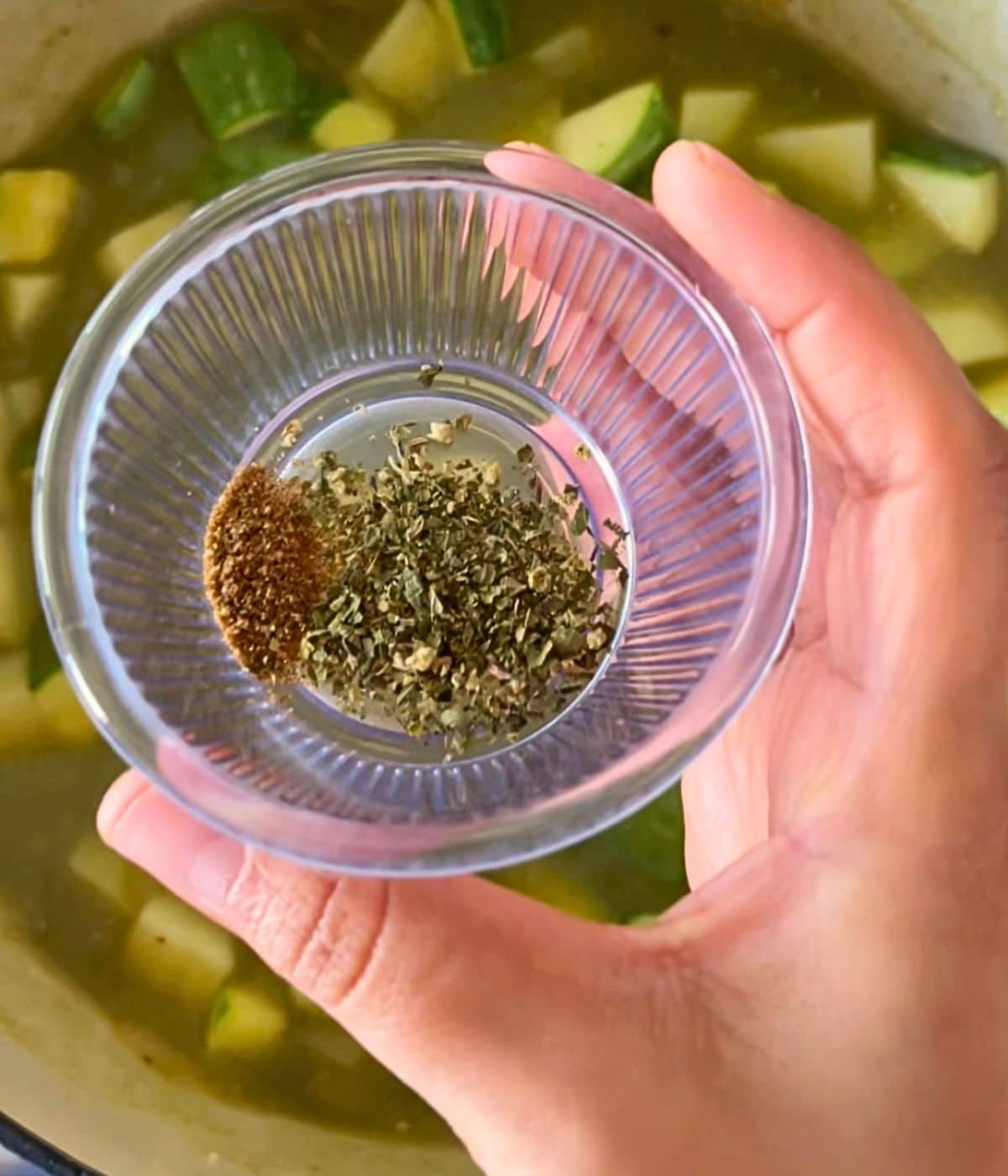 Oregano and cumin in a small bowl held over the pot.