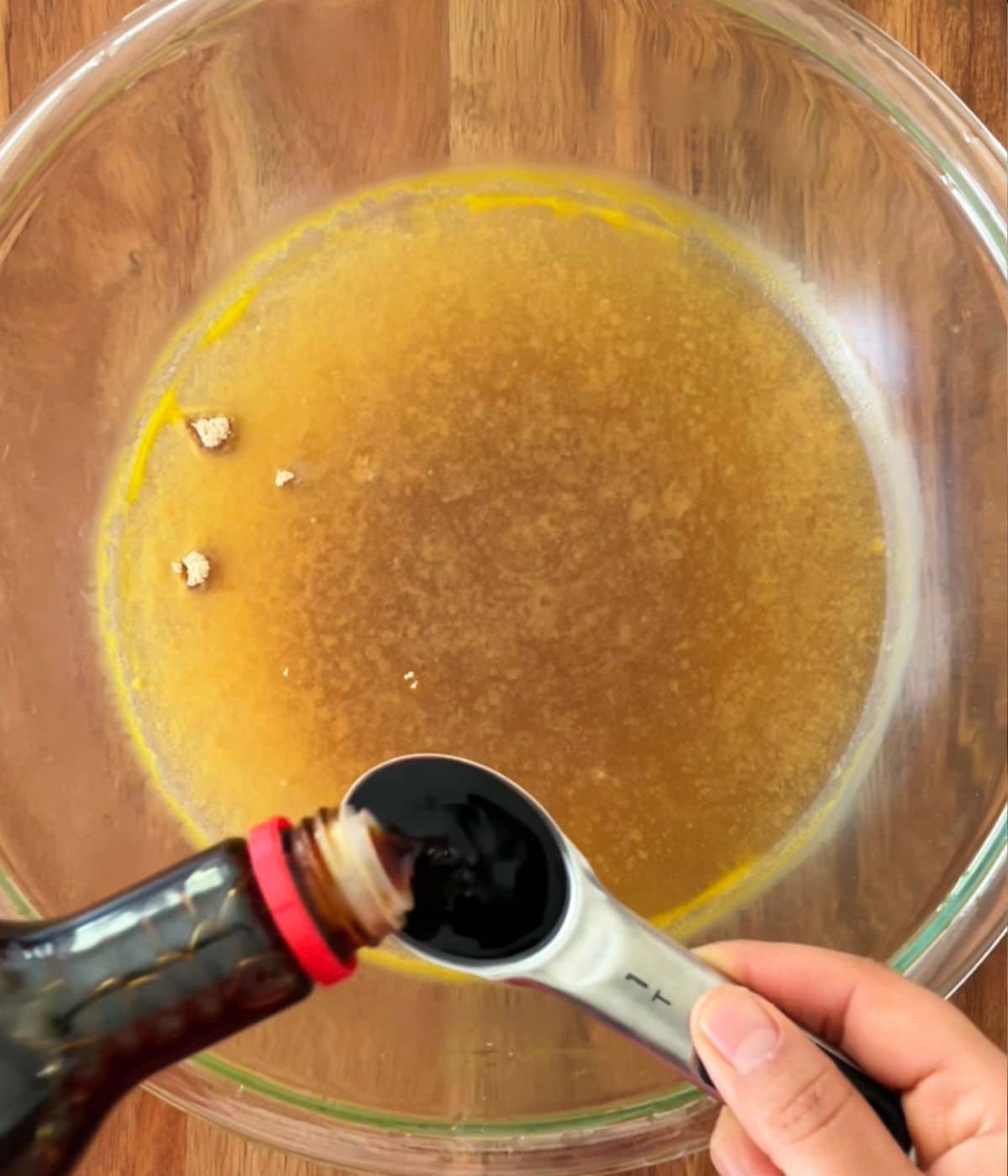 Vegetable broth in a bowl and soy sauce being added to it.