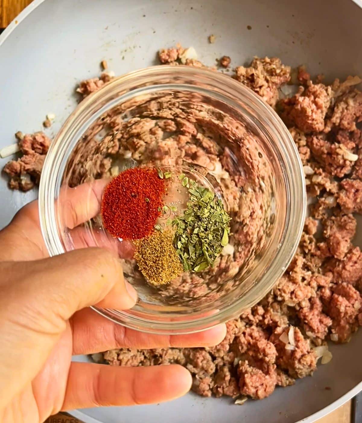 A small bowl of spices hovering over the skillet.