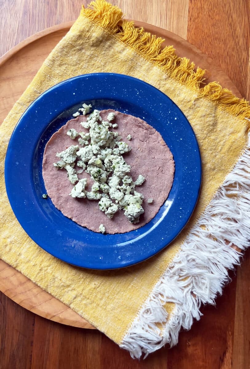 Requeson in a pink corn tortillas on a blue plate.