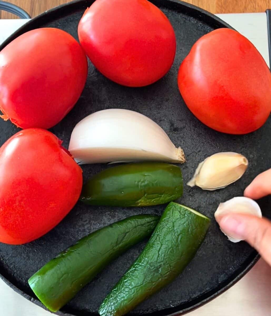 Tomatoes, onion, chiles, and garlic on a cast iron skillet.