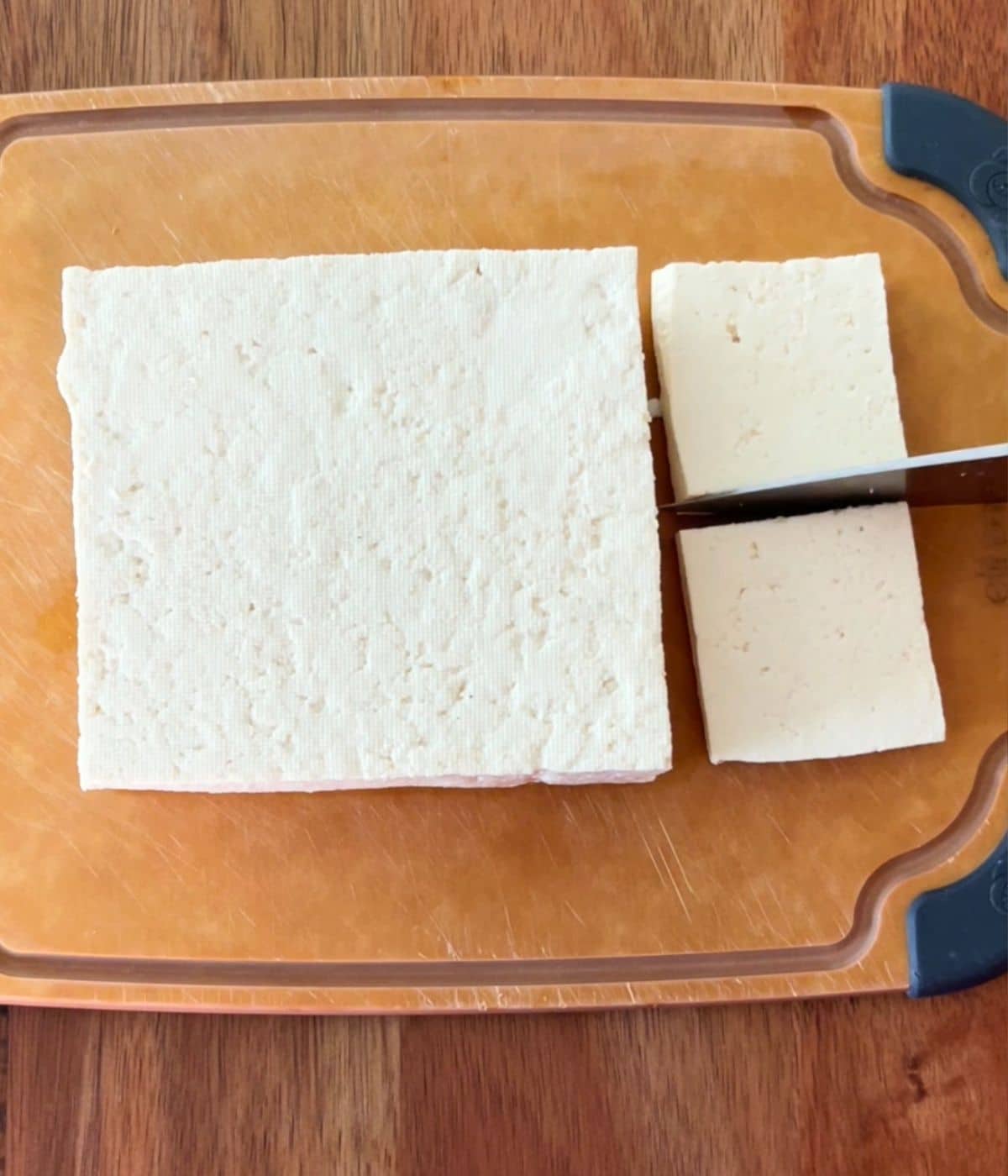 Tofu on a small cutting board being cut into squares.