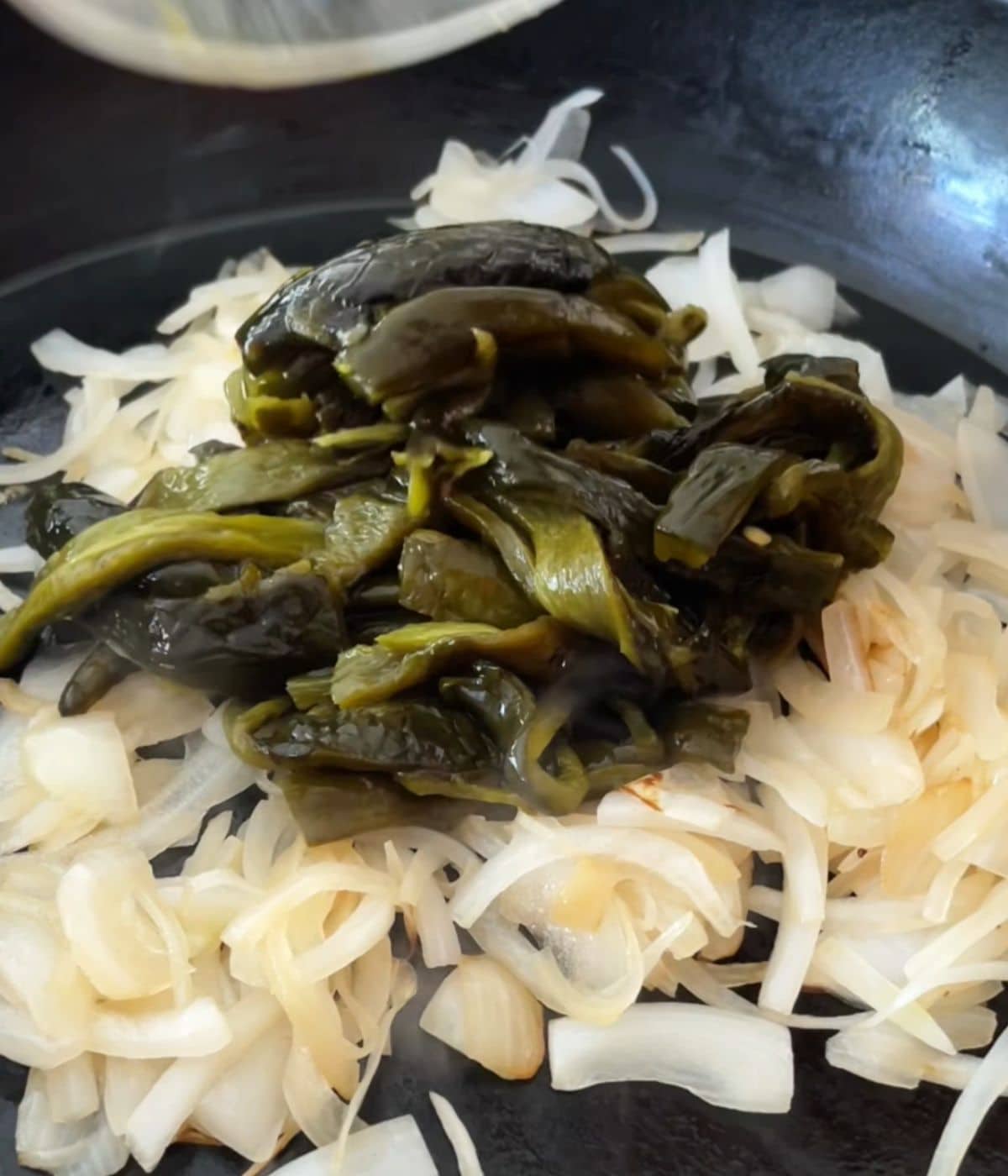 Roasted poblano peppers added to onions in a skillet.