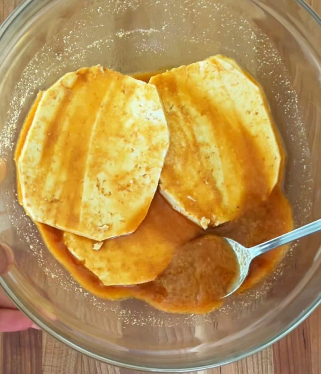 Tofu slices marinating in a glass bowl.