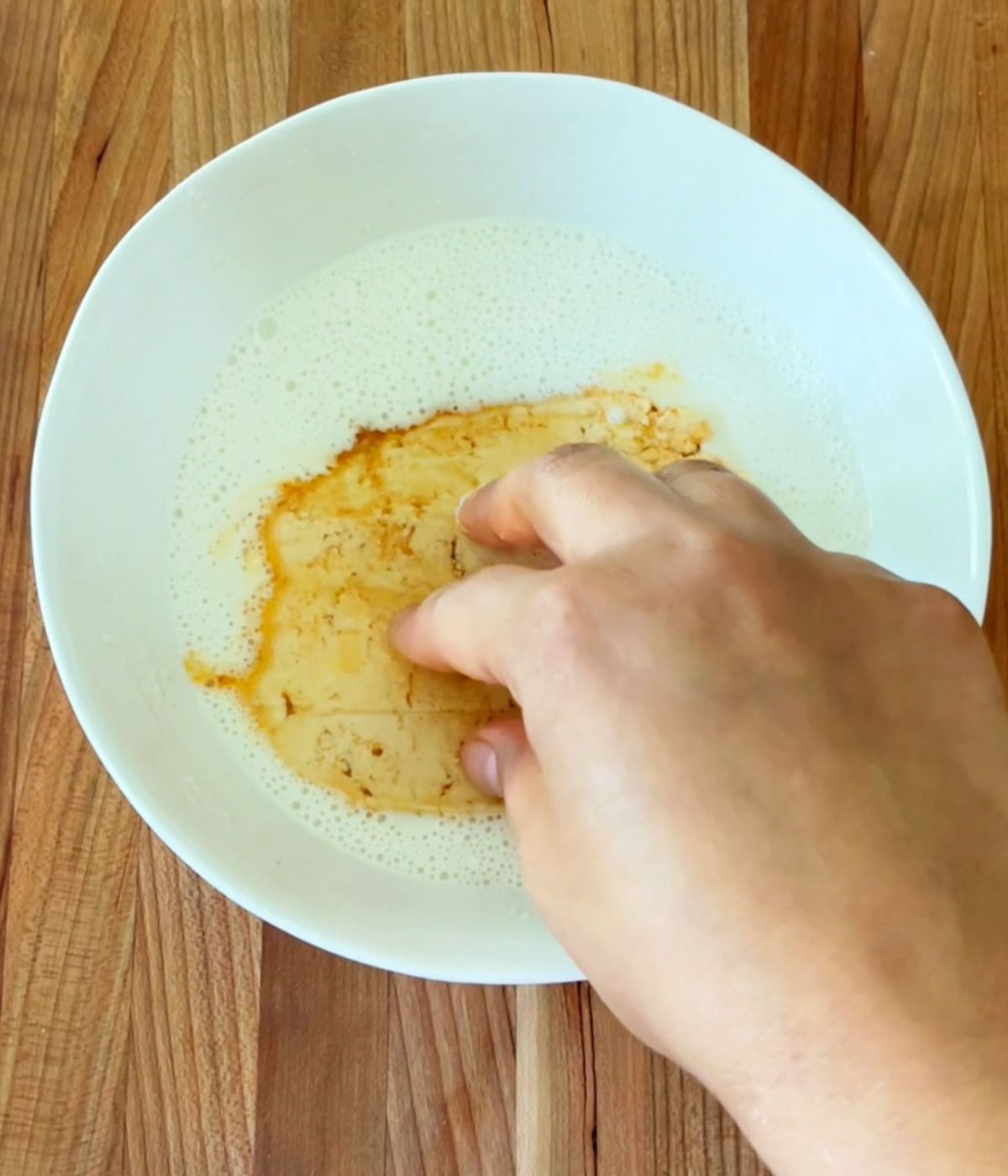 Tofu slice being dropped in a bowl with the batter.