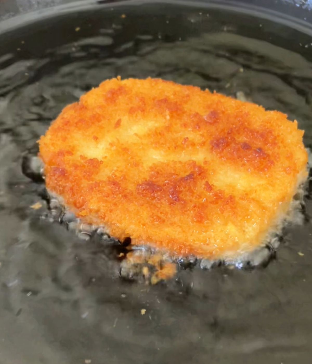 Tofu cutlet pan frying in black skillet.