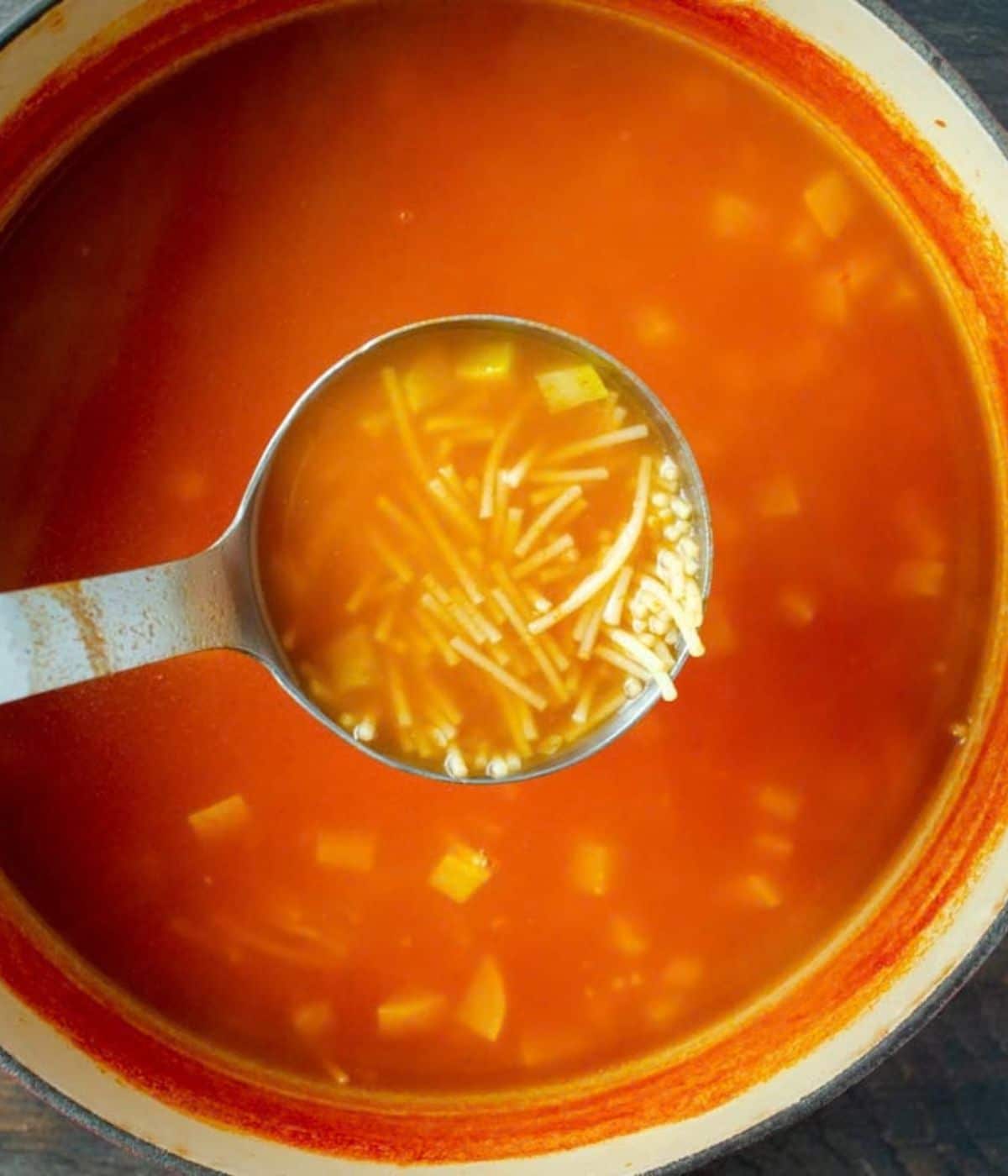Sopa de fideo in a large pot with a ladle lifted to the camera.
